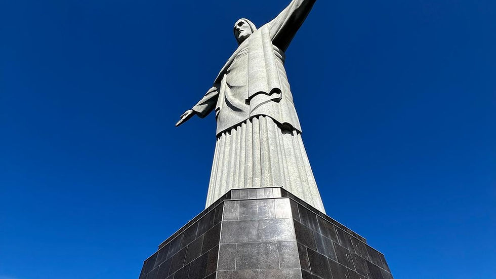 Statue of Christ the Redeemer with outstretched arms against a clear blue sky. Viewed from below, the stone structure is prominent and imposing.