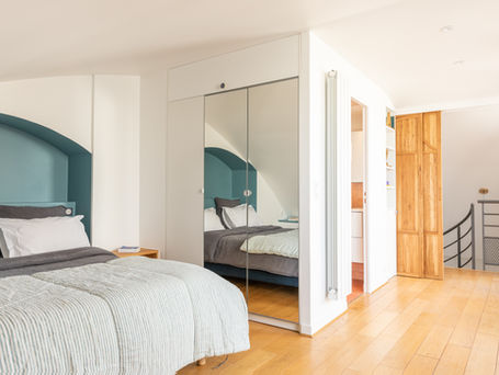 Aménagement d'un appartement duplex avec création d'une suite parentale à l'étage avec salle d'eau et WC, un espace dressing et des rangements sous pente pour optimiser chaque espace. Création d'une tête de lit niche arrondie, réalisation d'une porte coulissante double en chêne massif. Conception : ARCHITED, Architecture intérieure Paris