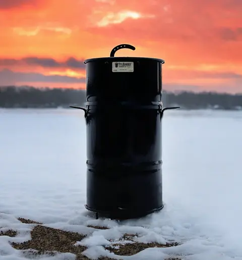 pit barrel cooker stood up in snow against sunset background