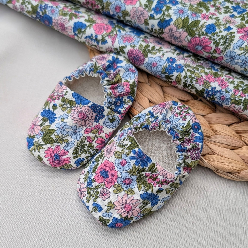 Pair of reversible cotton baby slippers showing a cream tonal print on one side and a blue and pink floral print on the rever