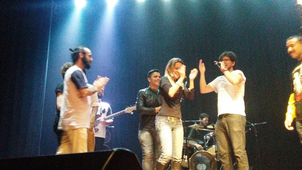 Grupo de músicos aplaudindo no palco durante performance noturna iluminada