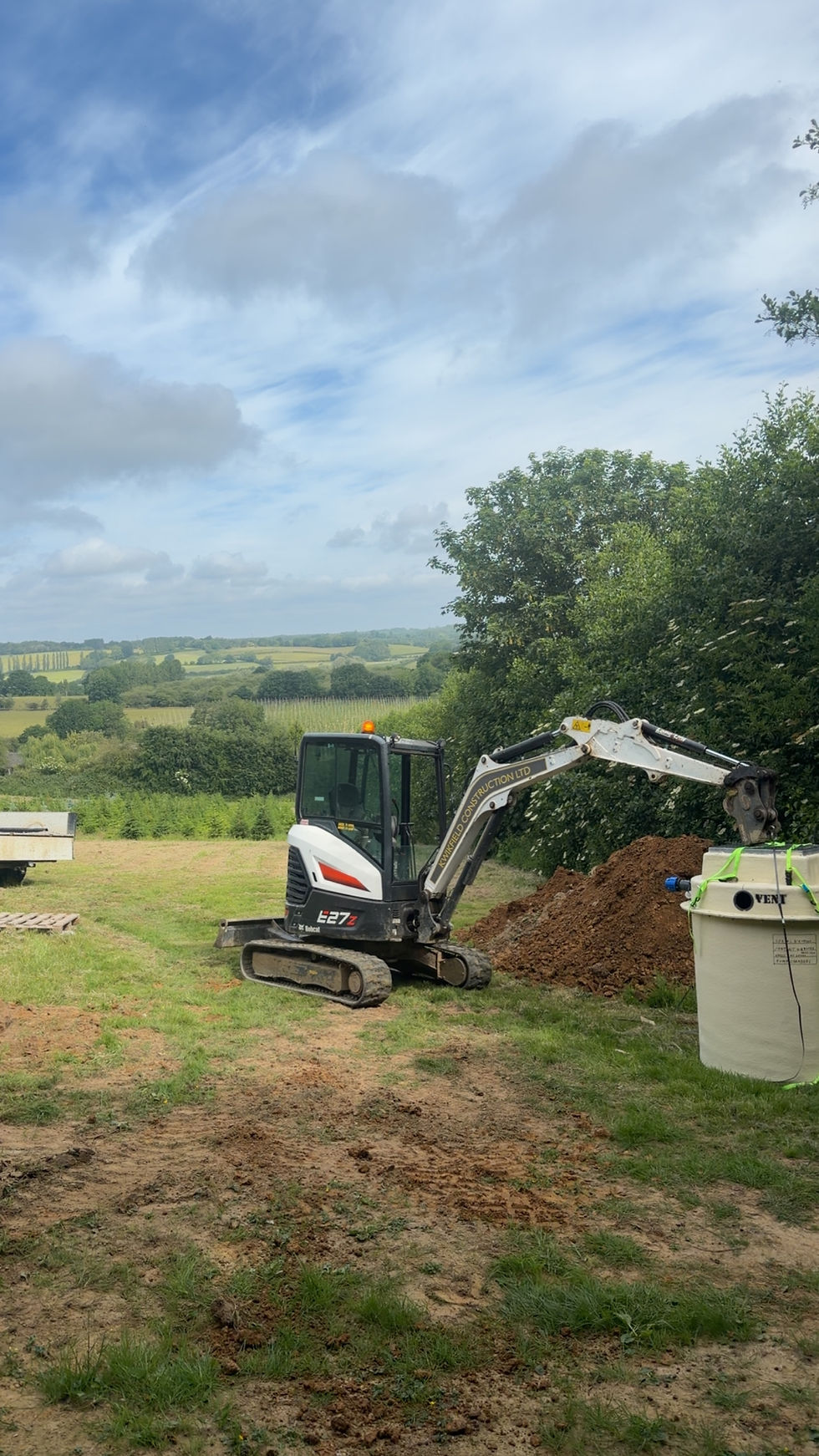 Small Bobcat excavator digging near a tank in a rural field