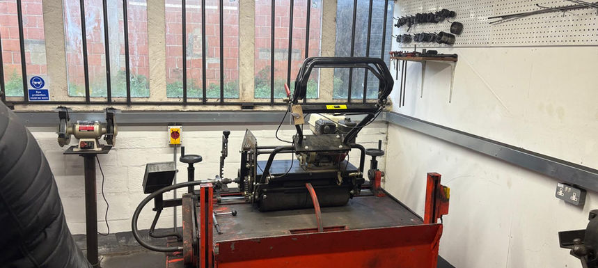 A professional cylinder mower sits on a red sharpening rig in a workshop with barred windows