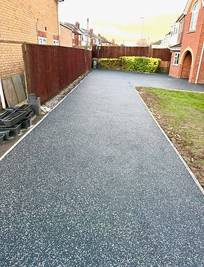 Finished dark grey resin bound driveway path winding next to a green grass verge