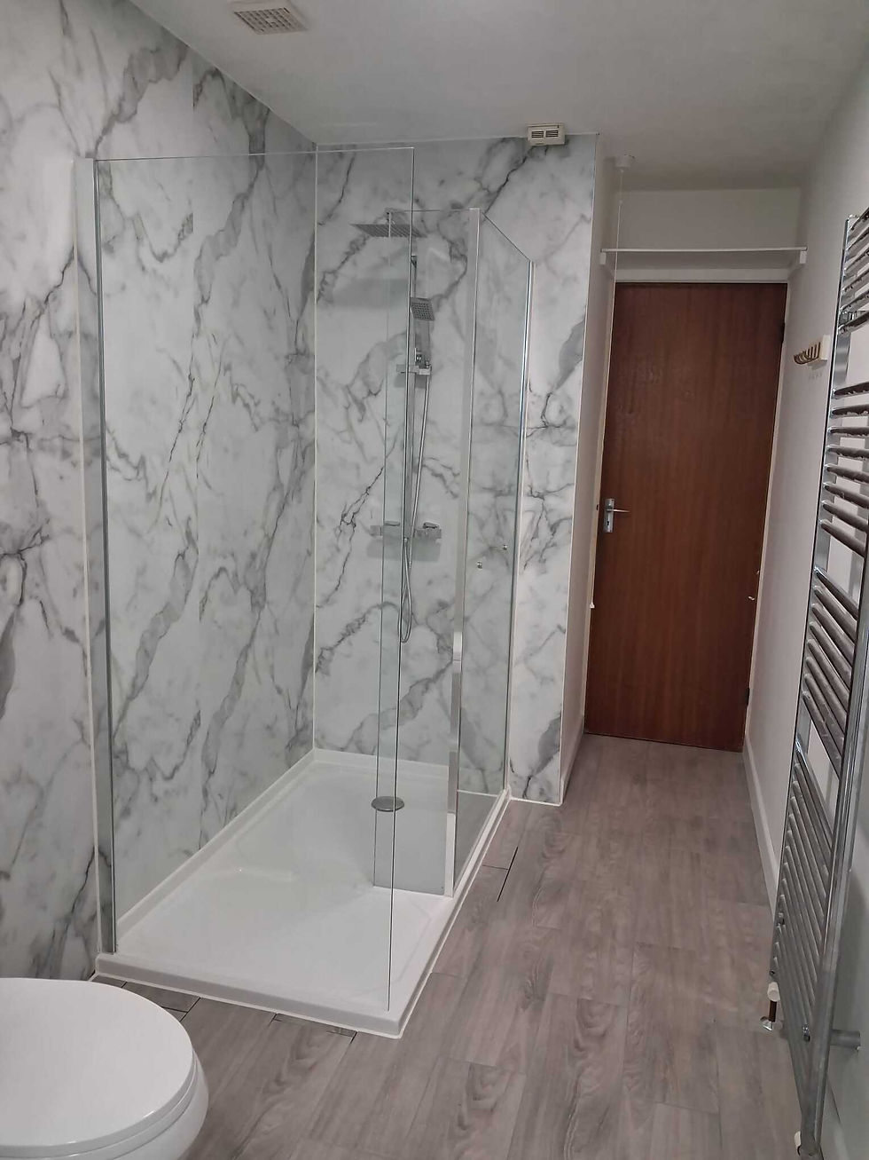Modern bathroom with a glass shower, wooden vanity with sink, and towel on a heated rail.