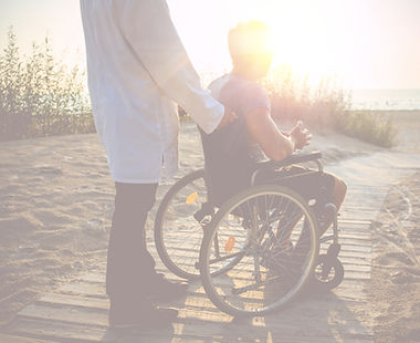 Man supporting an individual in wheelchair at the beach
