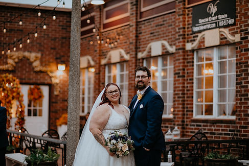 Bride and groom smiling in front of rustic brick building at Kansas City wedding venue.