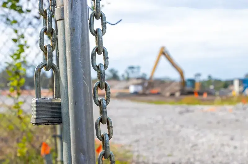 Close-up of a padlock and chain securing a construction site gate with machinery in the background, symbolising site security