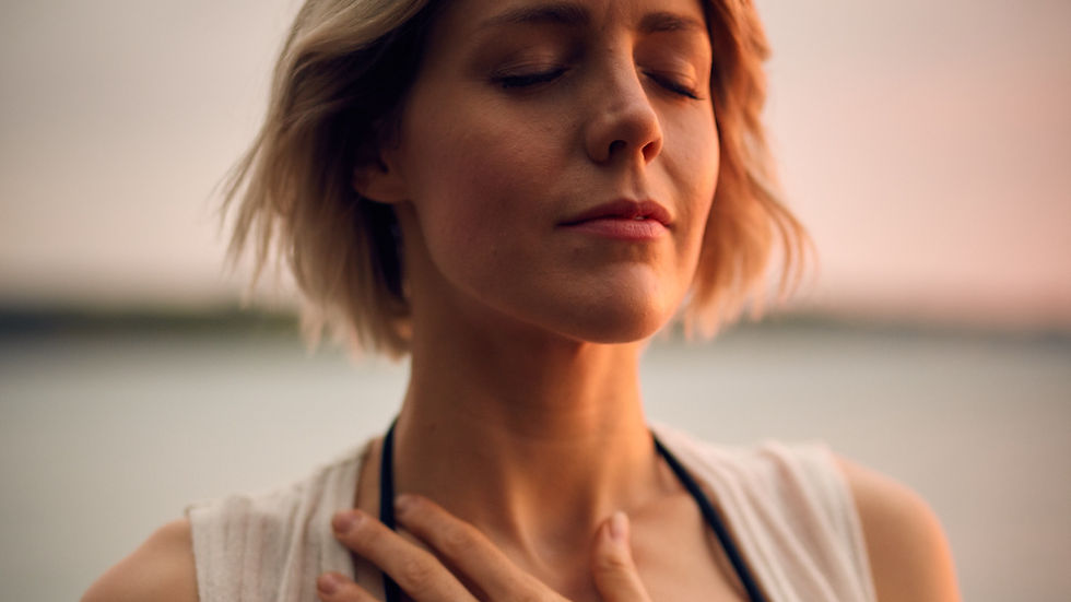 Woman with short hair closes her eyes, hand on chest, in a peaceful pose. Soft sunset light in the background, creating a calm mood. Connecting to IFS Self energy.