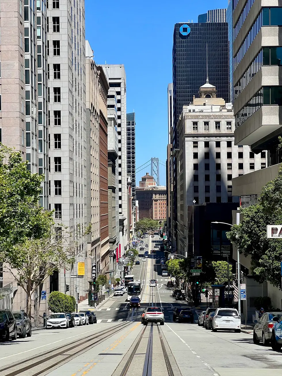 Downtown San Francisco street descending between tall buildings toward the Bay Bridge.