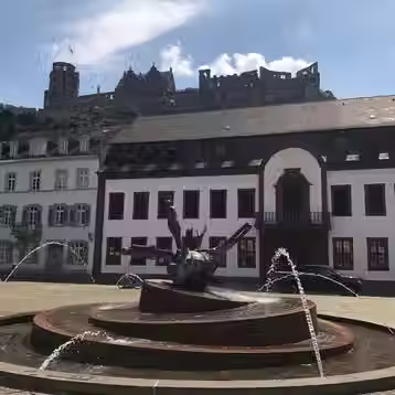 A fountain in Heidelberg’s Karlsplatz with the castle above the buildings.