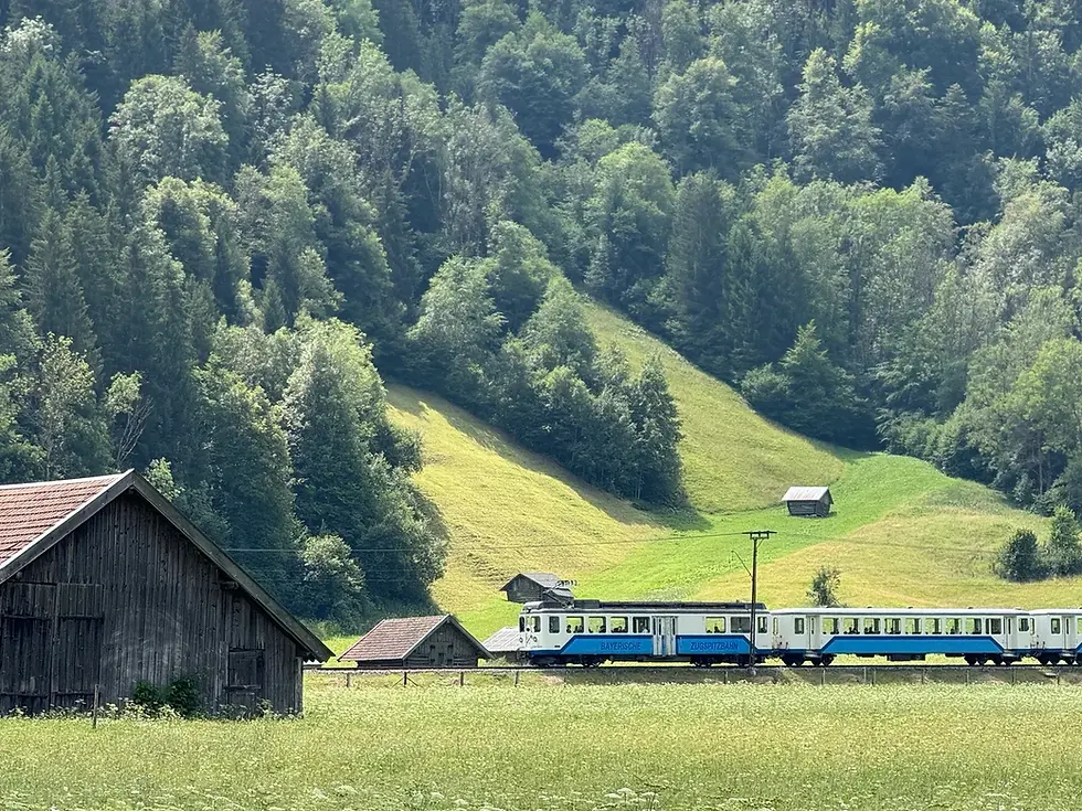 Zugspitzbahn train passing through green Alpine meadows and wooden barns near Garmisch-Partenkirchen