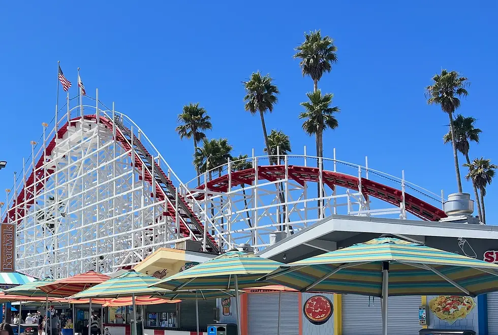 Red and white Giant Dipper roller coaster at the Santa Cruz Beach Boardwalk beneath tall palm trees.