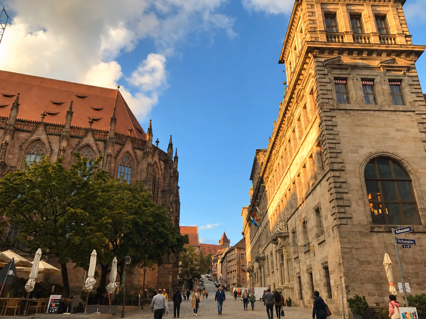 Historic stone buildings and pedestrians along Rathausplatz in Nuremberg’s Old Town, lit by the late-day sun.