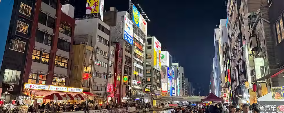 Illuminated buildings and signs above the Dotonbori canal in Osaka at night.