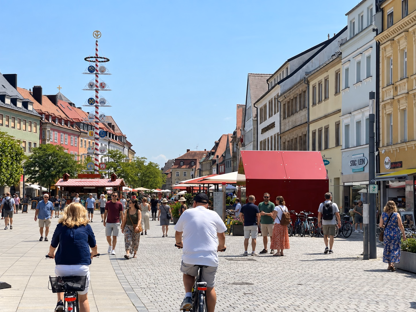 Pedestrians and cyclists moving through Bayreuth’s sunny pedestrian center lined with shops, cafés and historic buildings.