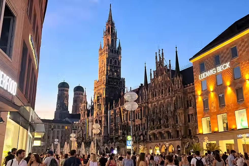 Munich’s Marienplatz at dusk, with the New Town Hall, Frauenkirche towers and a busy pedestrian crowd.
