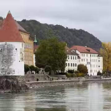 Passau’s white Schaibling Tower beside the Inn, with historic buildings and autumn trees along the promenade.