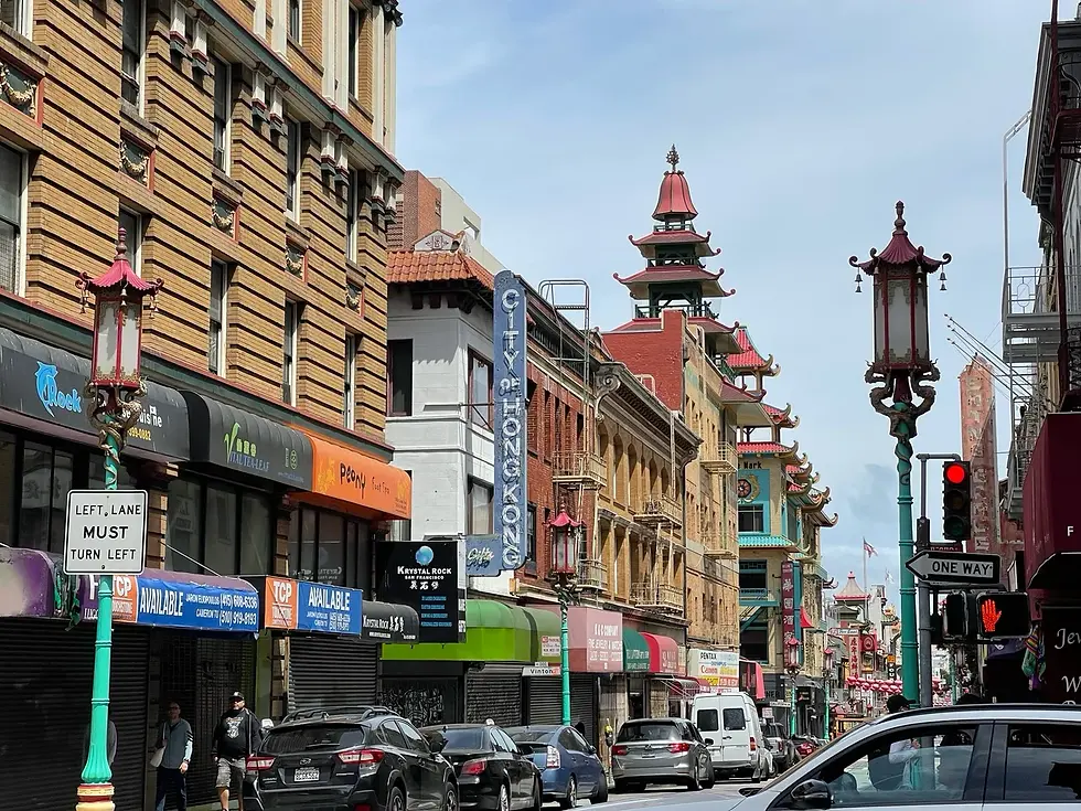 Chinatown street lined with shops, parked cars and pagoda-style rooftops.