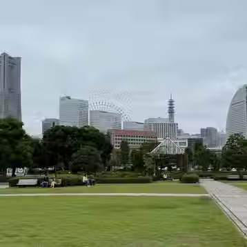 Green waterfront lawns and paths with Landmark Tower, the Ferris wheel and the sail-shaped InterContinental hotel behind.