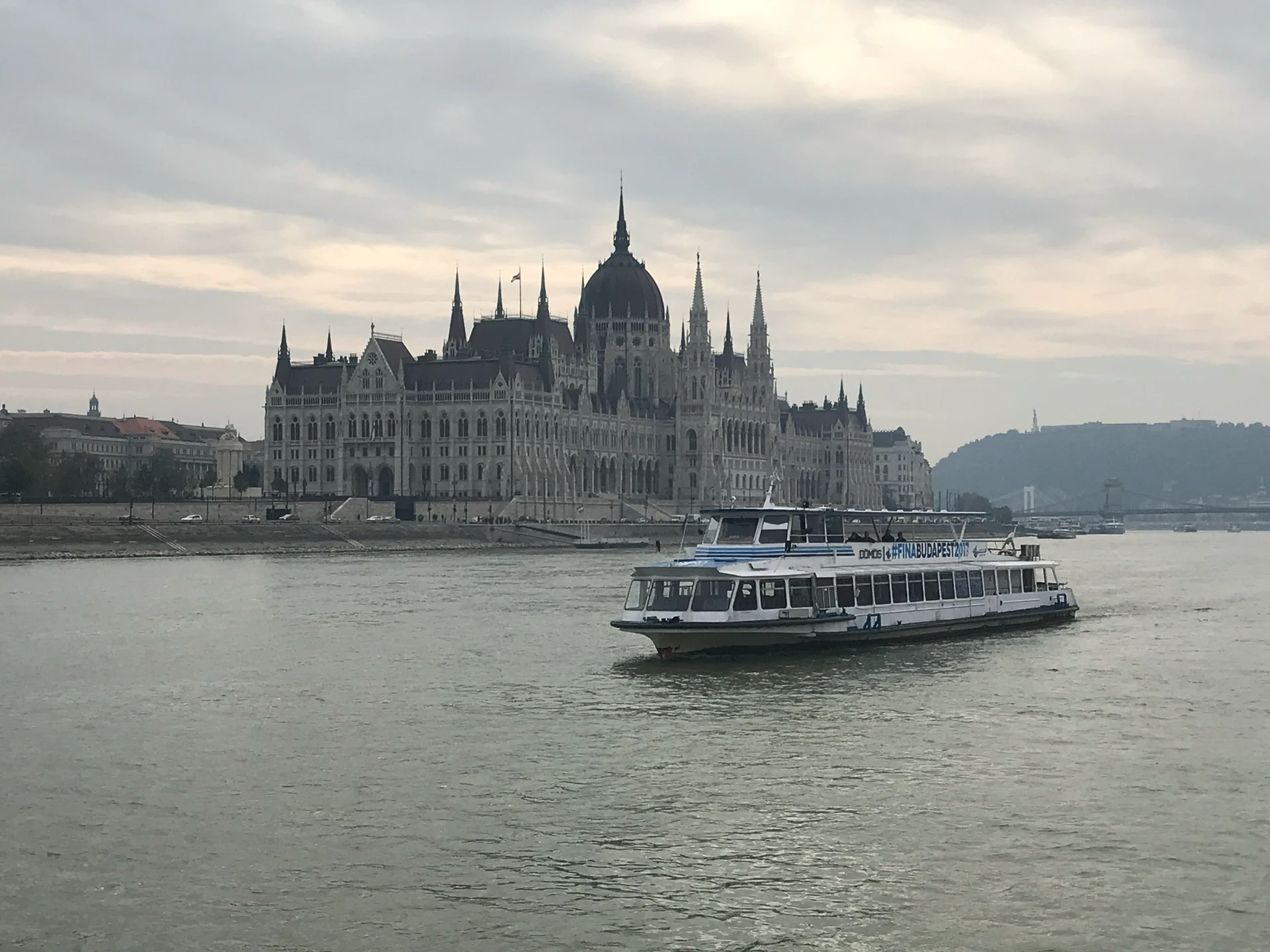 Budapest Parliament building on the Danube with a passenger boat, marking the final stop of the Munich-to-Budapest journey.