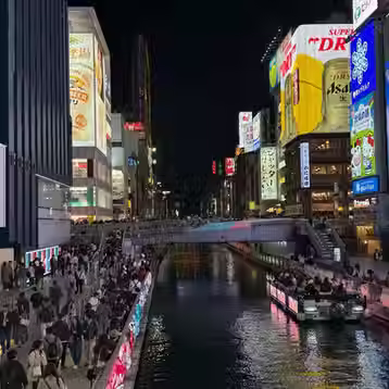 Bright neon signs and illuminated buildings reflected in Osaka’s Dotonbori canal at night.