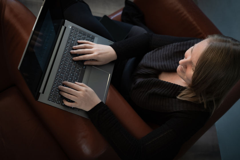Agata Staniak sitzt auf einem braunen Ledersessel und arbeitet an einem Laptop. Die Hände sind auf der Tastatur positioniert, während die Person auf den Bildschirm schaut. Die Umgebung ist dezent beleuchtet und vermittelt eine entspannte Arbeitsatmosphäre.