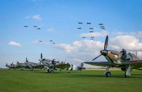 Side view of Spitfire planes lined up on a field, with Spitfires flying in formation above.