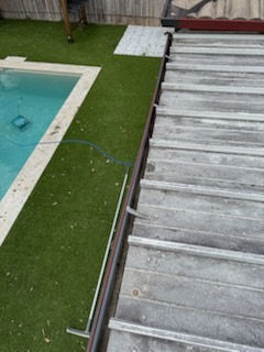 Close-up of freshly cleaned gutters on a poolside residential property with artificial turf garden.
