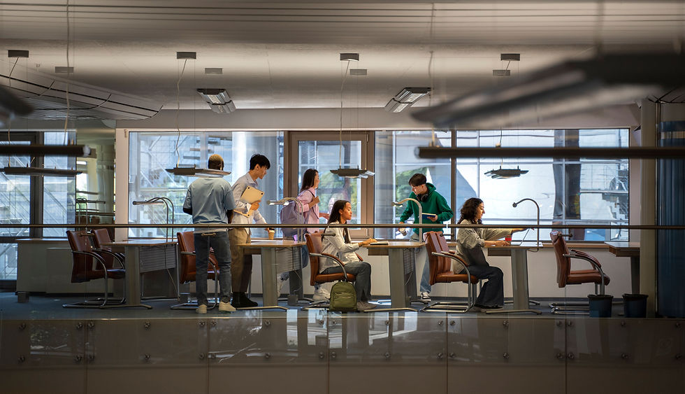 Personas jóvenes estudiando y conversando en un espacio moderno de trabajo colaborativo con escritorios y lámparas.