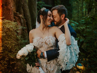 Romantic forest wedding portrait at TreeHouse Point near Seattle, Washington, featuring a bride in a sculptural floral lace gown embracing her groom among towering evergreens, with wedding planning, coordination, and design by Your Perfect Bridesmaid.