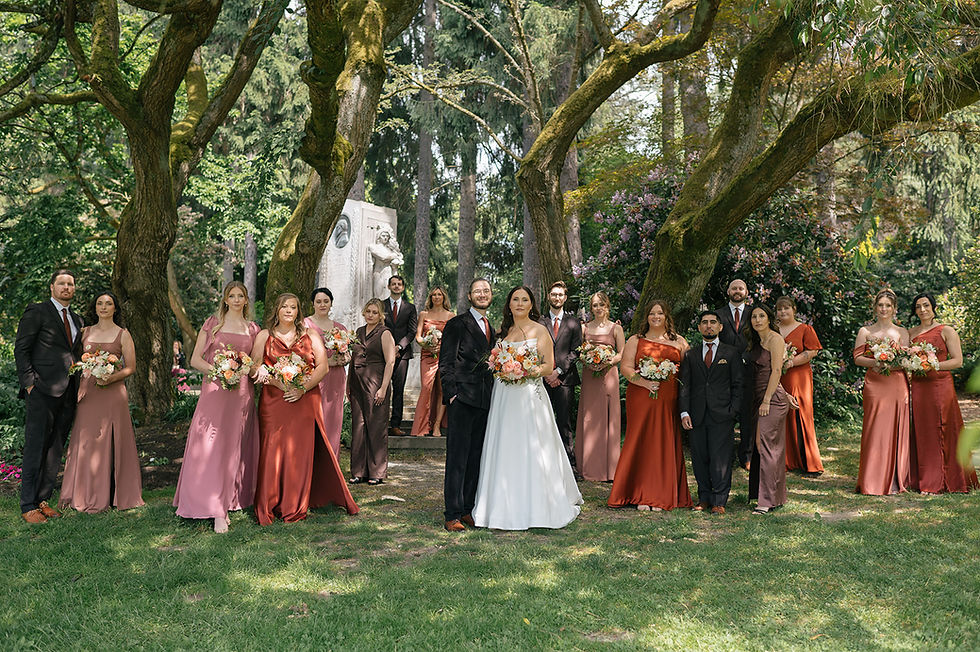 Bride and groom posing with their bridal party in a formal, stoic arrangement, showcasing a romantic palette of rosy hues, dusty rose, terracotta, and soft sunset tones against a lush park background.