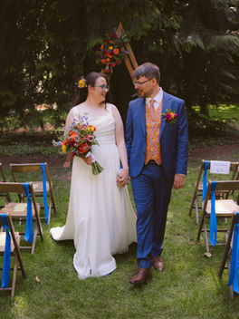 Bride and Groom walking hand in hand down the aisle at IslandWood, surrounded by colorful jewel toned florals in the forest meadow.