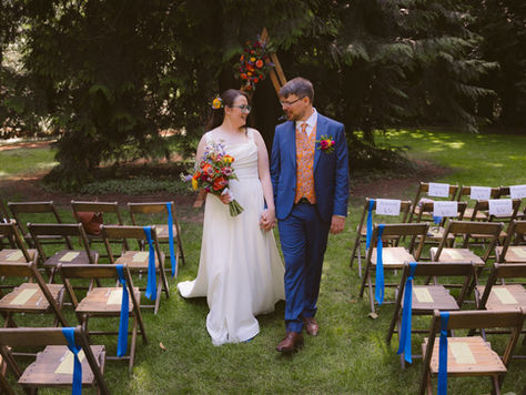 Bride and Groom walking hand in hand down the aisle at IslandWood, surrounded by colorful jewel toned florals in the forest meadow.