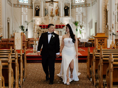 Couple walking down the aisle at St. Mary Catholic Church in Mt. Angel, Oregon during a Catholic wedding ceremony, with floral petals scattered along the aisle and soaring church architecture.