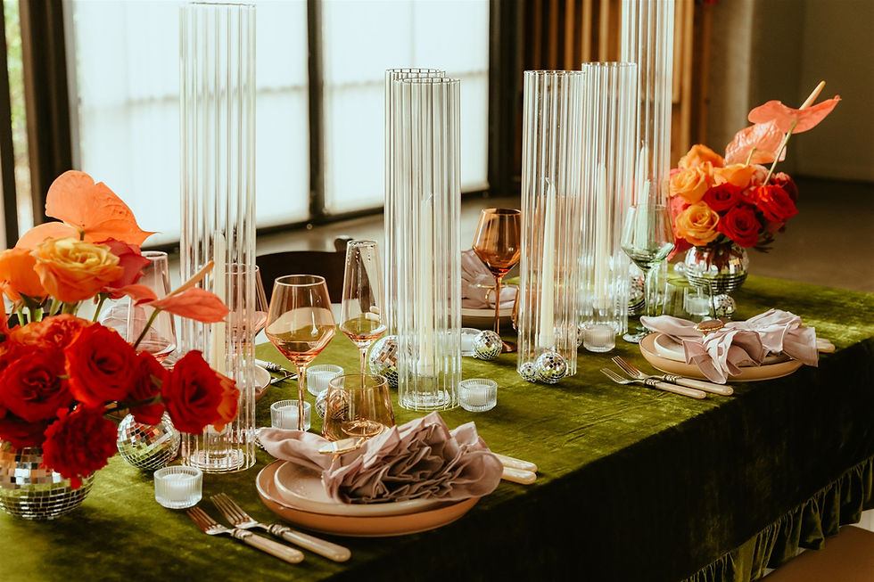 Jewel-toned wedding reception tablescape at The Paseo featuring deep green velvet linens, vibrant red and orange florals, blush napkins, glass candleholders, and disco ball accents.