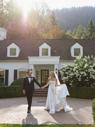 Bride and groom holding hands in front of Fox Hollow Farm during their garden wedding, lovingly gazing at each other as the bride gently holds her dress in a romantic black-tie celebration.