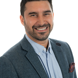 A smiling man wearing a blue business suit with red pocket handkerchief against a white background.