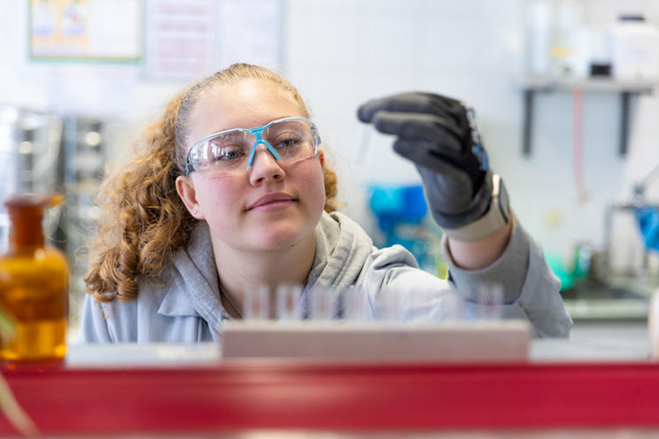 Junge Frau mit Schutzbrille betrachtet Reagenzglas in einem Laborgebäude.