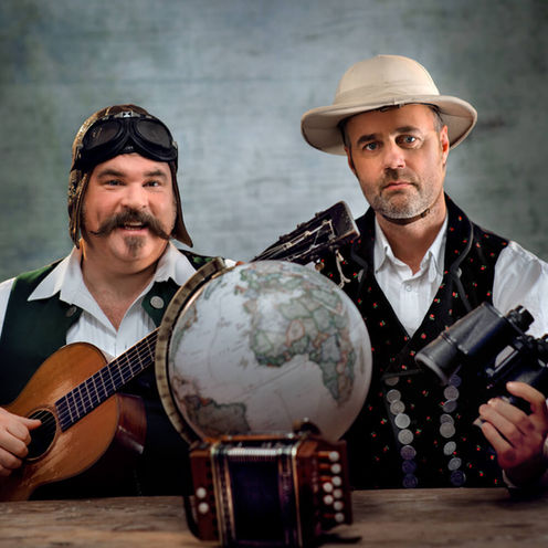 Künstler Fotoshoot: Zwei Personen mit Hüten sitzen vor einem Globus. Eine Person hält eine Gitarre.