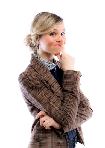 Portrait einer Kabarettistin in braunem Blazer mit weißem Hintergrund.