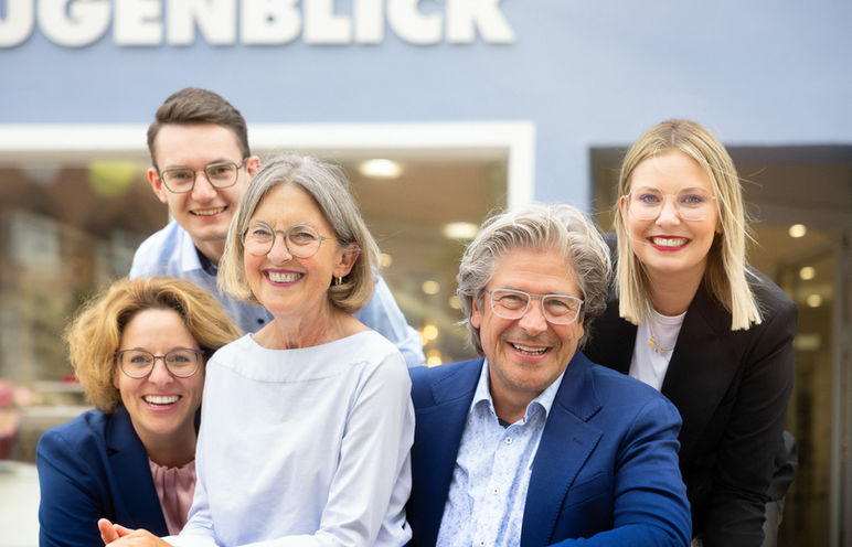 Fünf lächelnde Mitarbeiter eines Augenoptik-Geschäfts vor Schriftzug UGENBLICK.