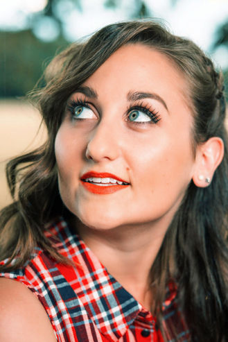 Junge Frau mit roten Lippen und kariertem Hemd blickt nachdenklich auf.