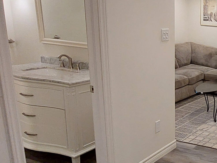 Basement washroom with a white vanity, marble countertop, and modern lighting, showcasing a clean and functional design.