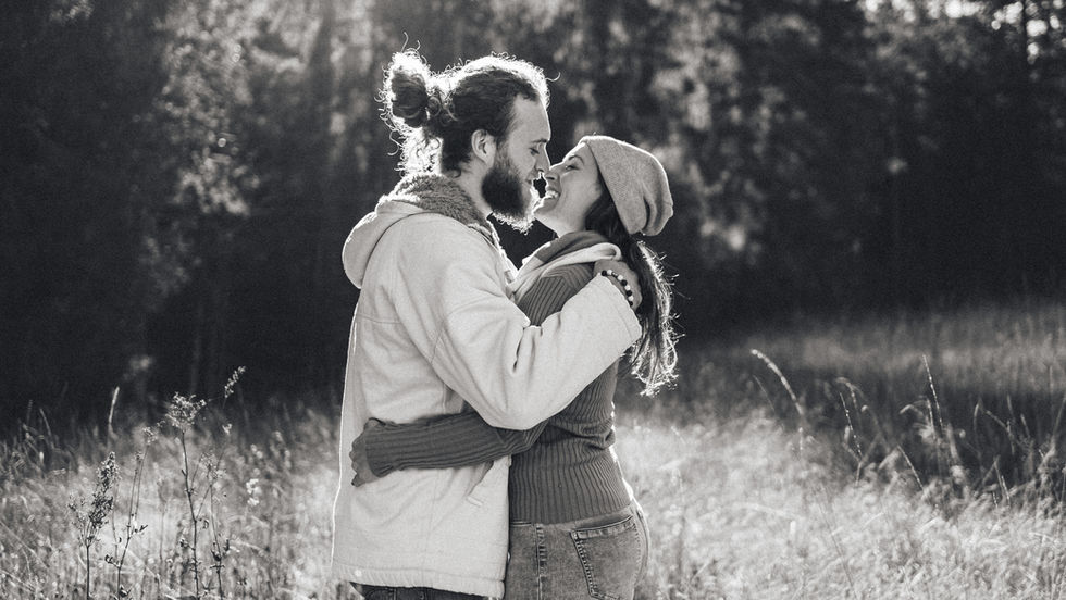 Liebevoll kuschelndes Paar auf einer herbstlichen Wiese im Gegenlicht in Schwarz Weiss