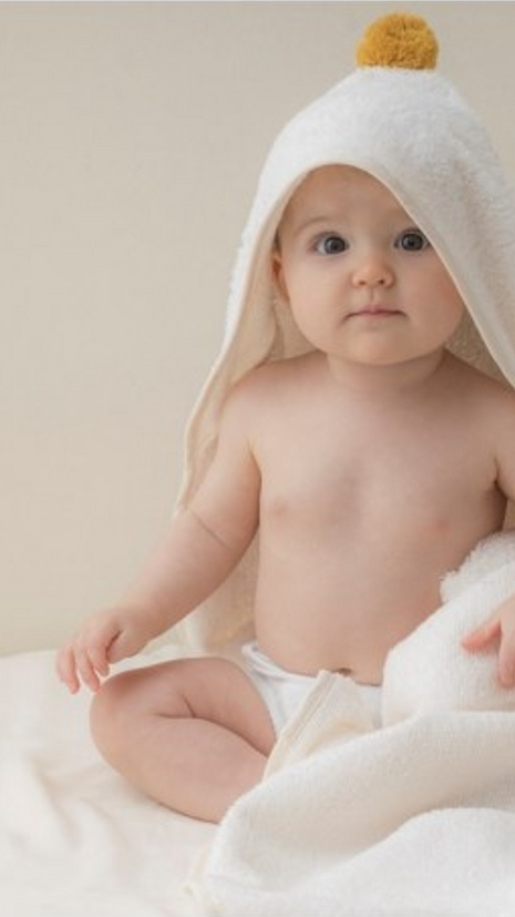 bébé portant une cap de bain en éponge blanche avec un pompon jaune