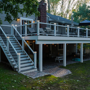 Two-story deck with stairs and railing, surrounded by trees.