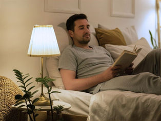 A man unwinds in bed with soft lighting and a book as he prepares for a good night's sleep