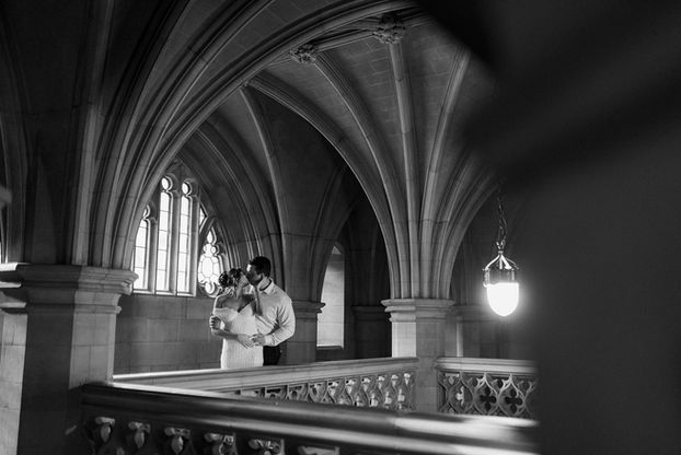 Black and white University of Toronto engagement photo of a couple embracing near historic arches