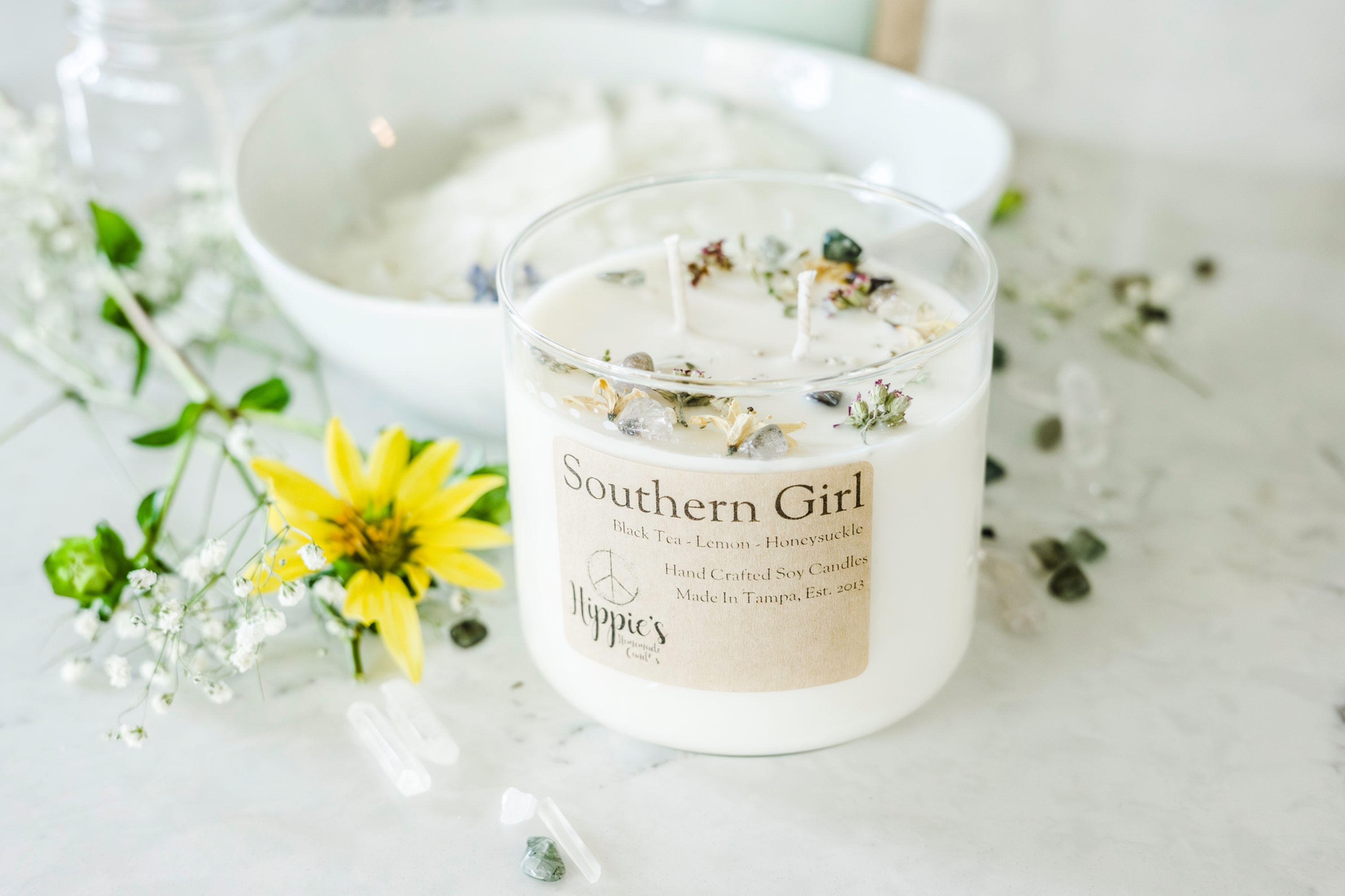 A white candle with flowers and crystals on top with the words southern girl on the label, surrounded by flowers and crystals. 
